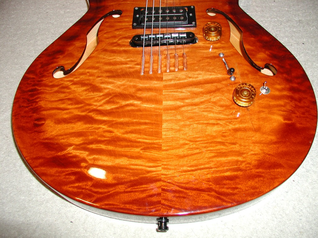Close-up of an orange sunburst hollow-body electric guitar body with pickups and knobs