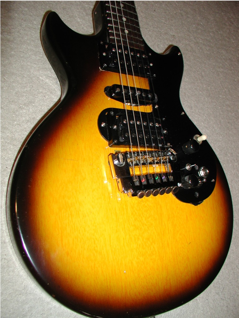 Close-up of an electric guitar body with a sunburst finish, black hardware, and pickups, on a light background