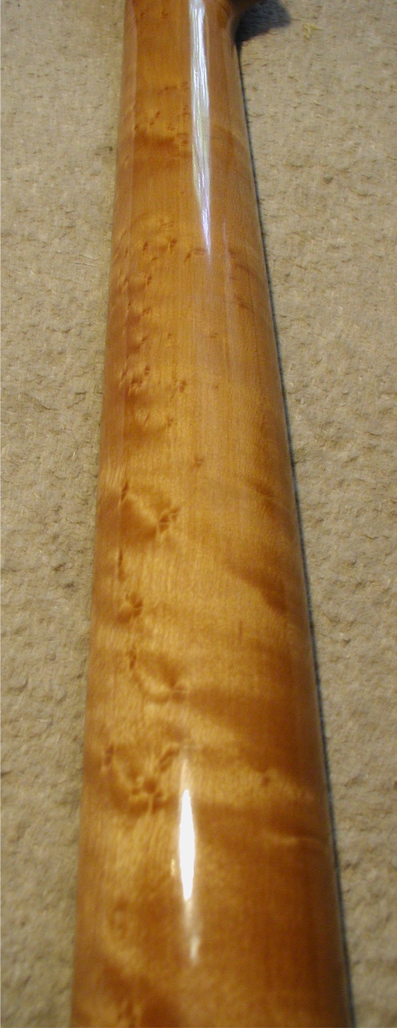 Close-up of a glossy wooden guitar neck with figured grain, warm amber tones